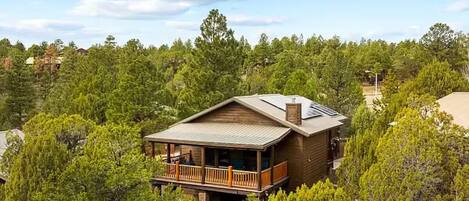 A wooden cabin with a balcony, surrounded by dense forest.
