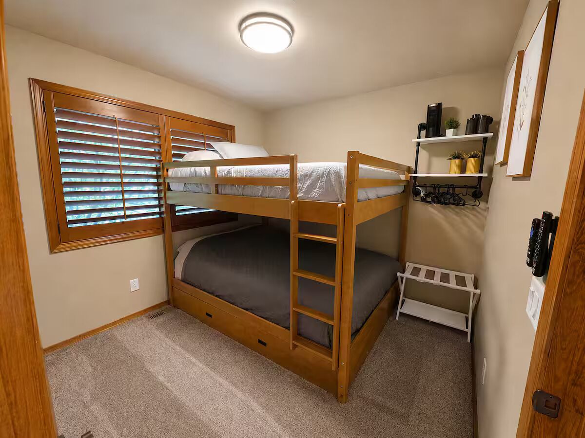 A bunk bed room with a window, a shelf with plants, and a door.