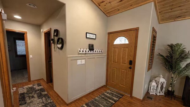 A hallway with wooden flooring, a coat rack, a door with a glass panel, and a potted plant.