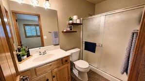 Un bagno con un mobile vanitario in legno, un water bianco, un box doccia in vetro e uno specchio con illuminazione.