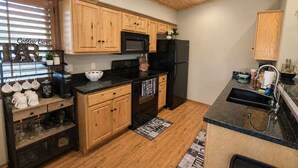 A kitchen with wooden cabinets, a black refrigerator, a microwave, and a coffee station.