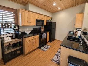 A kitchen with wooden cabinets, a black refrigerator, a microwave, and a coffee station. - NEW - The Cozy Bison (Show Low)