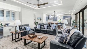 A modern living room with a sofa set, a coffee table, and a dining area with a view. - Waterfront Fun, Private Beach, Pool, Spa & Games - Laguna Lake House - Roelens (Cape Coral)