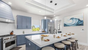 A modern kitchen with a central island, bar stools, and a large window. - Waterfront Fun, Private Beach, Pool, Spa & Games - Laguna Lake House - Roelens (Cape Coral)