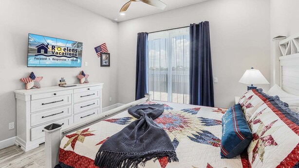 A bedroom with a bed, a dresser, a television, and a ceiling fan. - Waterfront Fun, Private Beach, Pool, Spa & Games - Laguna Lake House - Roelens (Cape Coral)