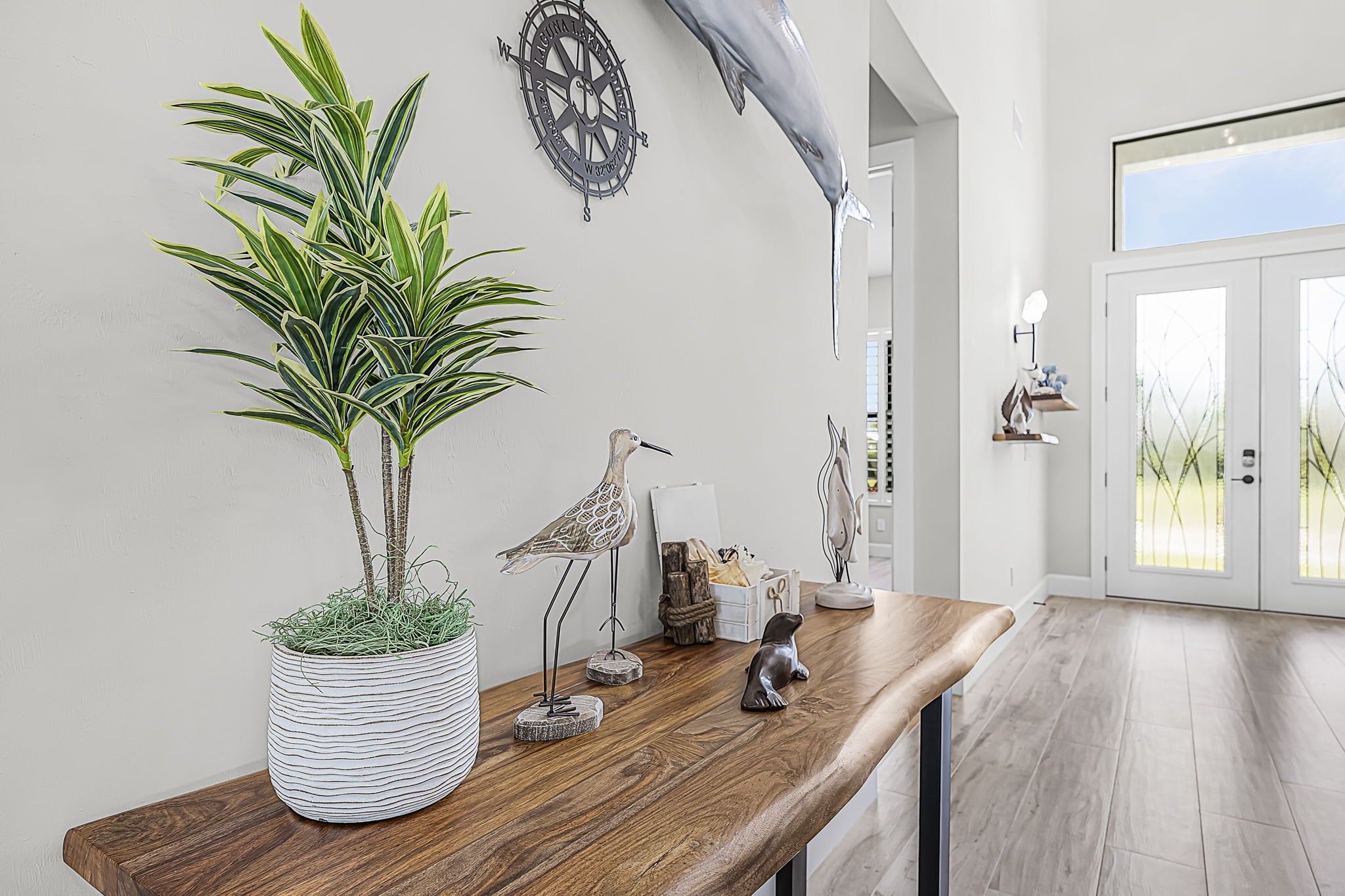Ein modernes Interieur mit einem Holztisch, einem Topfpflanzen, einem Wandkompass und einer Delphinskulptur.