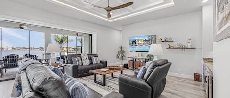 A spacious living room with a large window, a ceiling fan, and a flat-screen TV mounted on the wall.