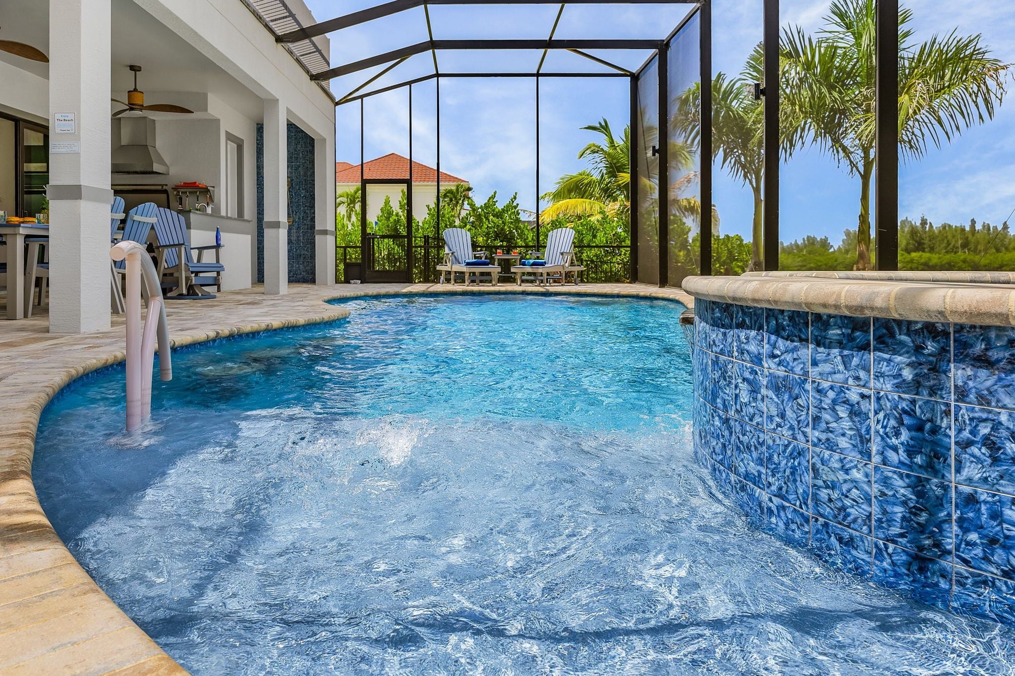 A swimming pool with a tiled edge, lounge chairs, and a covered area with a ceiling fan.