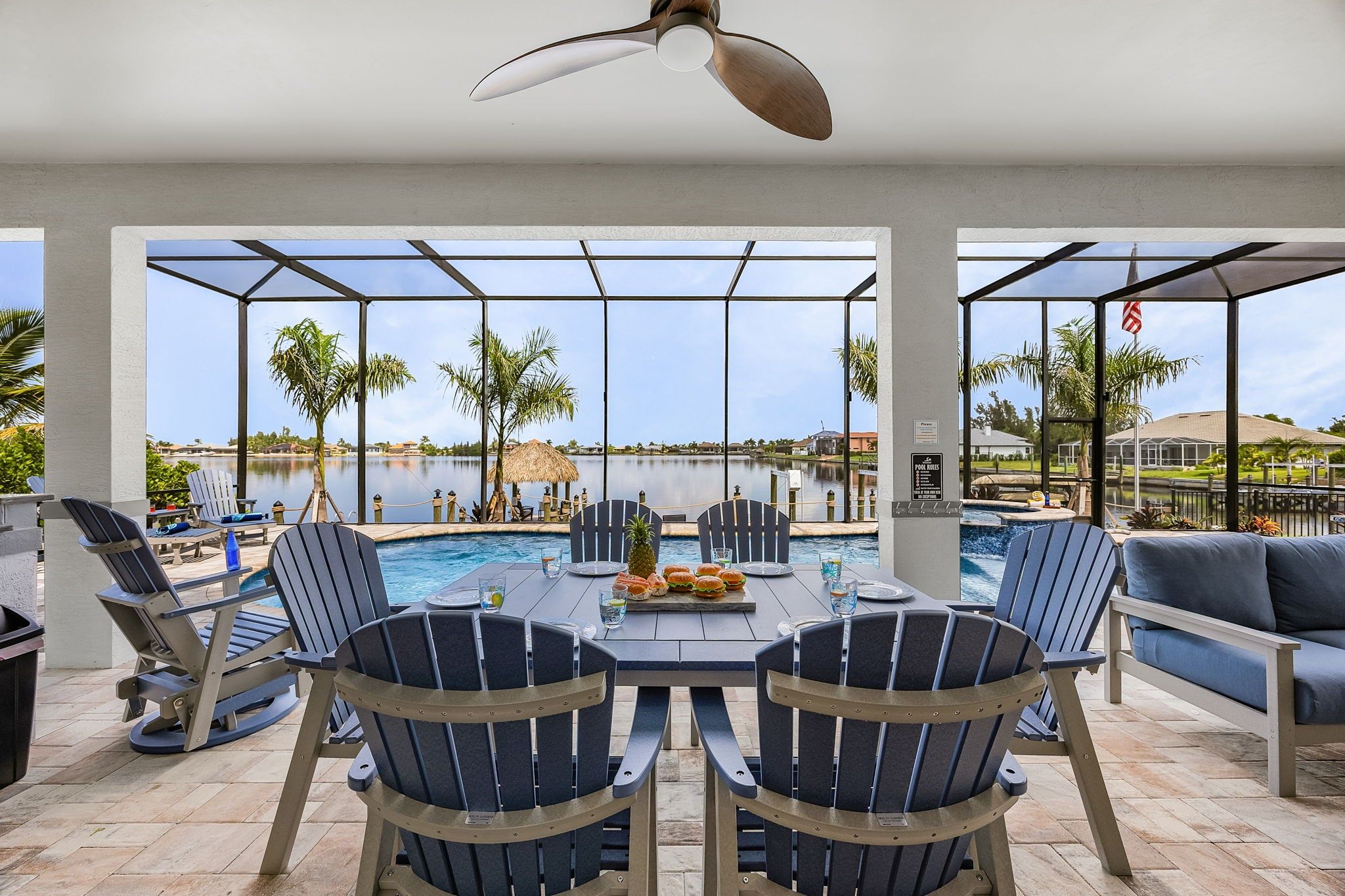 A poolside dining area with a table, chairs, and a view of a lake.