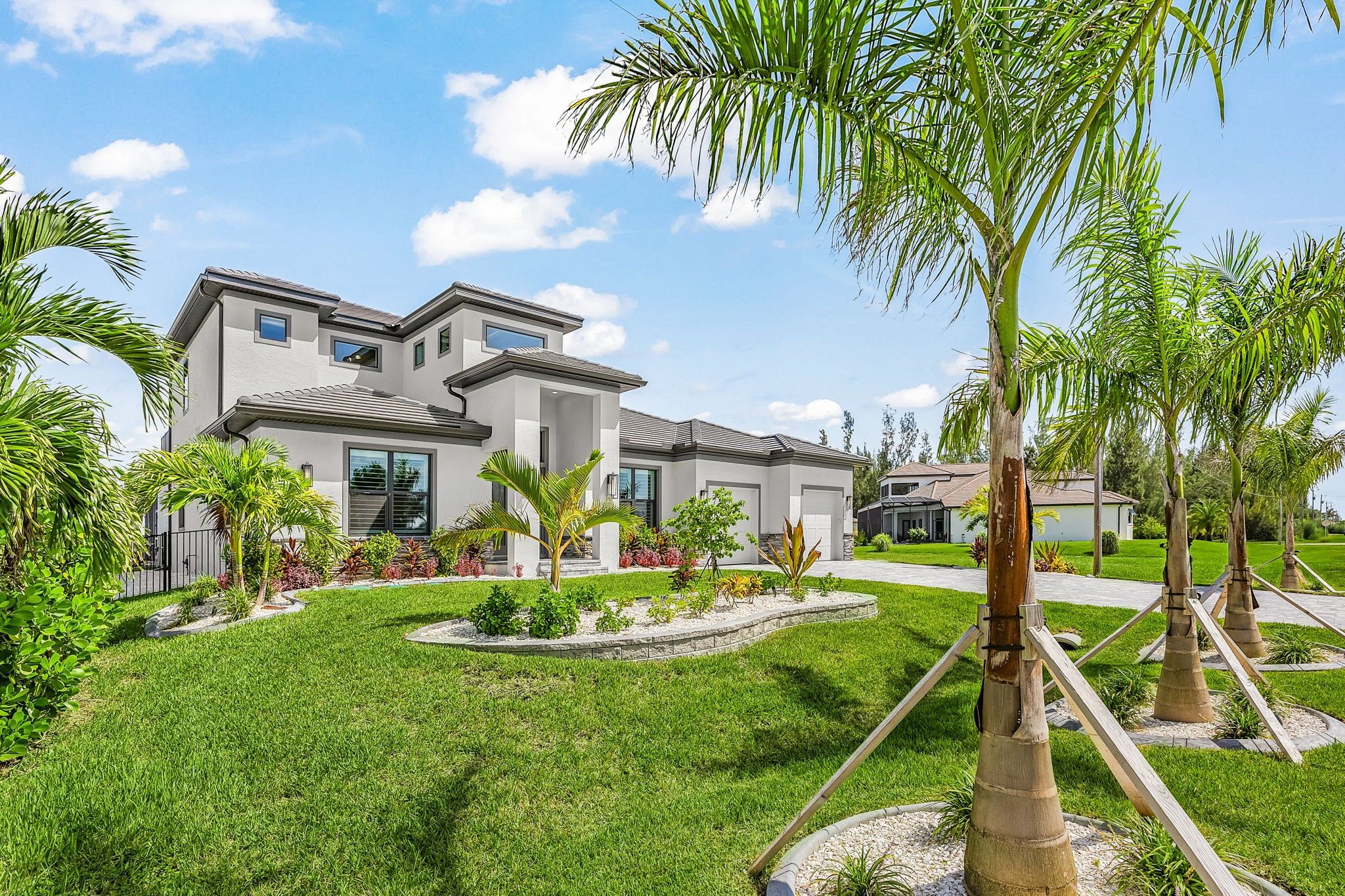 A modern two-story house with a well-maintained lawn and palm trees.
