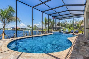 Ein Pool mit geschwungener Kante, umgeben von einer überdachten Terrasse mit Stühlen und Blick aufs Wasser.