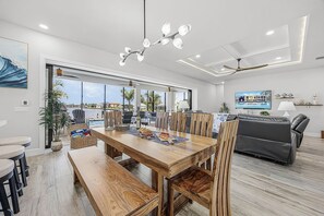 A spacious dining area with a wooden table and chairs, a pool view, and a modern ceiling fan. - Waterfront Fun, Private Beach, Pool, Spa & Games - Laguna Lake House - Roelens (Cape Coral)