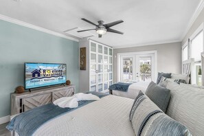 A hotel room with a bed, a television displaying a vacation ad, a ceiling fan, and a view of the outside. - Gulfside Fun, Pool Days & Waterfront Adventures Await - Coastal Oasis - Roelens (Fort Myers Beach)