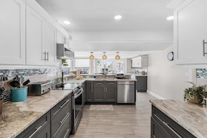 A modern kitchen with white cabinetry, stainless steel appliances, and a central island. - Gulfside Fun, Pool Days & Waterfront Adventures Await - Coastal Oasis - Roelens (Fort Myers Beach)