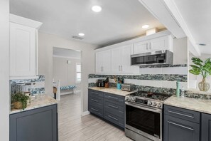 A modern kitchen with white cabinets, a stainless steel range, and a tiled backsplash. - Gulfside Fun, Pool Days & Waterfront Adventures Await - Coastal Oasis - Roelens (Fort Myers Beach)