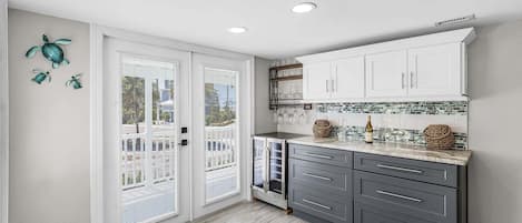 Cocina con armarios blancos, encimera de mármol y vistas a través de una puerta corrediza de vidrio.