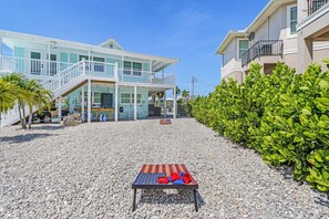 A two-story building with a covered outdoor area, a flag on the ground, and a well-maintained hedge. - Gulfside Fun, Pool Days & Waterfront Adventures Await - Coastal Oasis - Roelens (Fort Myers Beach)