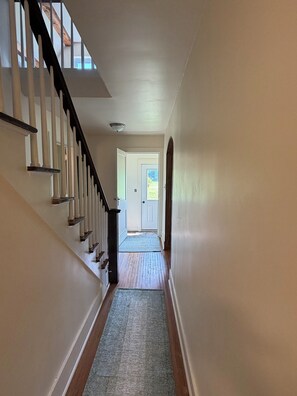A hallway with a wooden staircase, a door at the end, and a carpeted floor.