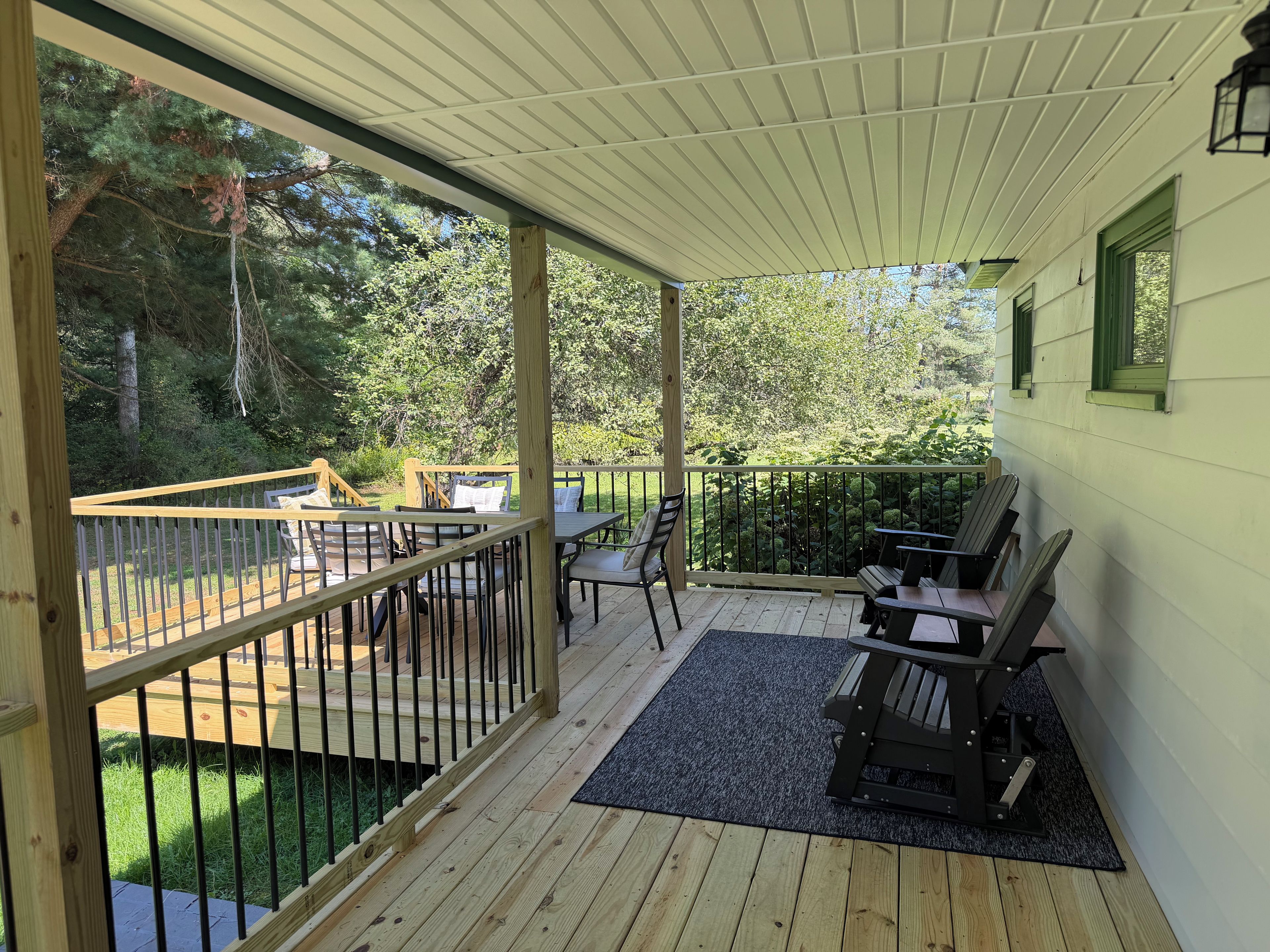 Eine überdachte Terrasse mit Sitzgelegenheiten im Freien, einem Holzgeländer und Blick auf die umliegende Natur.