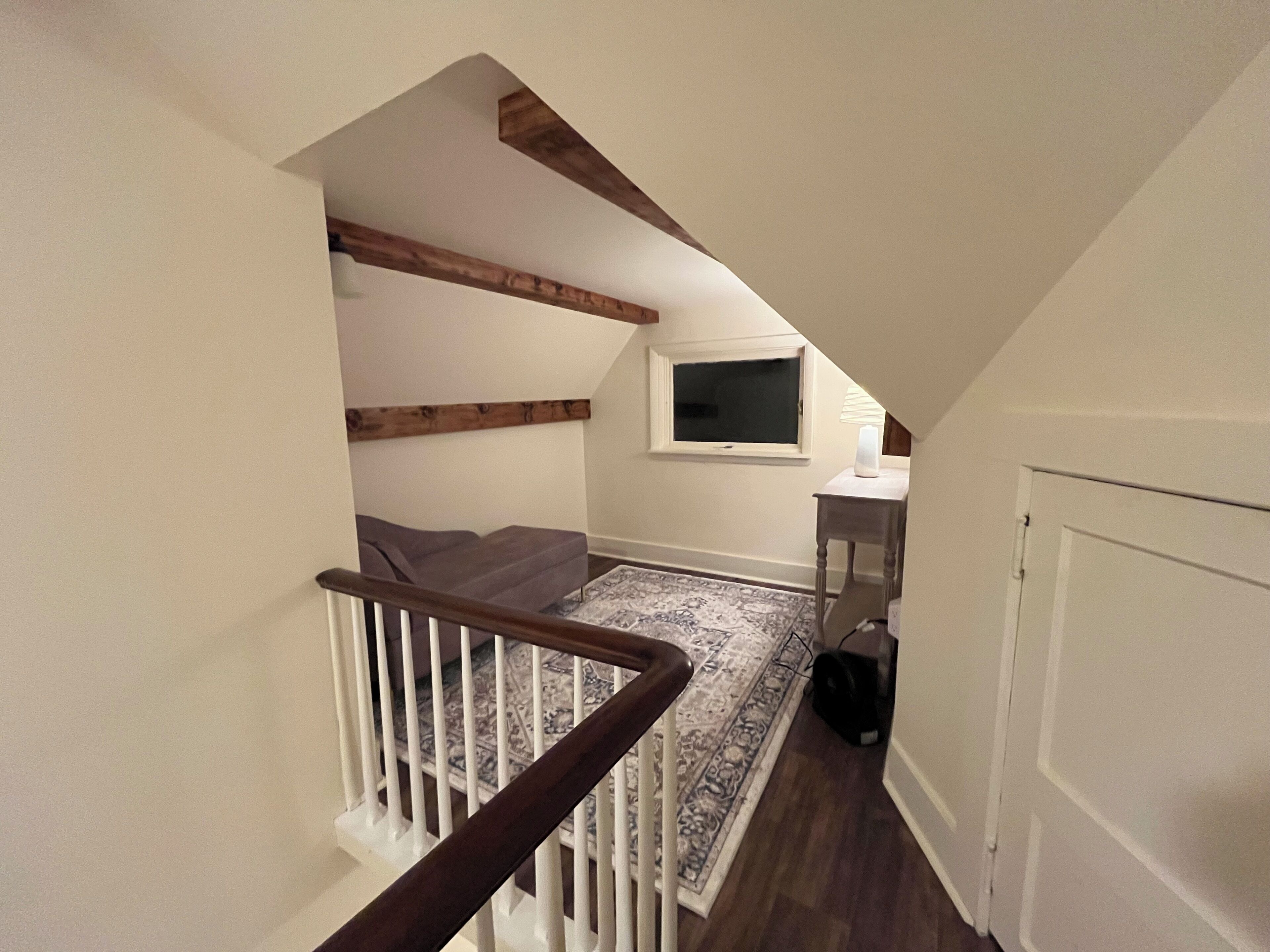 Una escalera con barandillas de madera que lleva a un rellano con un televisor y una pequeña mesa.