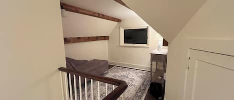 A staircase with wooden railings leading to a landing with a television and a small table.