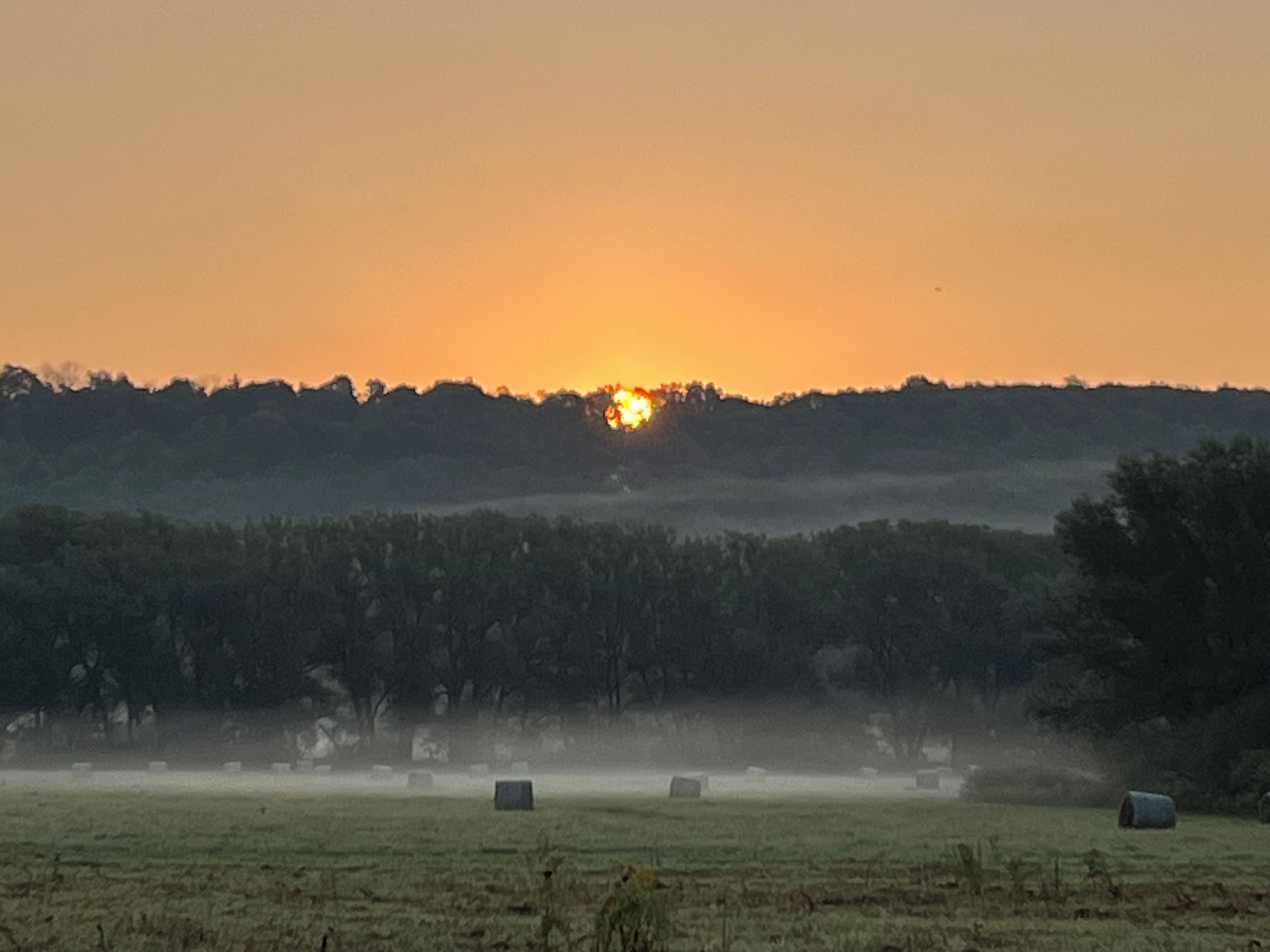 A field with hay bales and a sunset in the background.