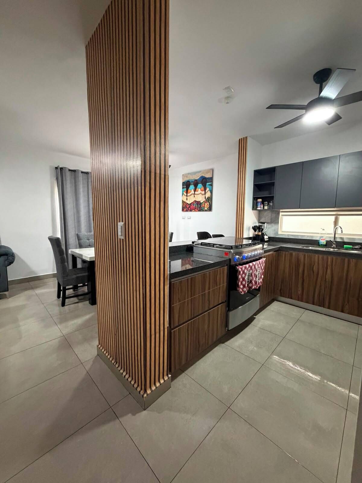 Une cuisine moderne dotée d’un îlot central, de meubles de couleur sombre et d’un ventilateur de plafond.