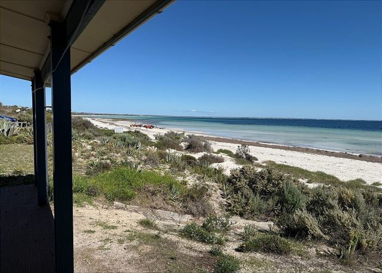 A coastal view from a covered area with a sandy beach and sparse vegetation.
