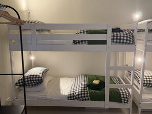 Et værelse med køjeseng, hvide sengetæpper og ternede puder.