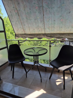 A balcony with two chairs and a small table, a mesh fence, and a floral-patterned awning. -  Acropolis Museum Grand Mansion (Athina)