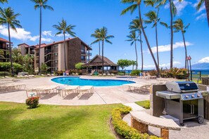A pool area with lounge chairs, a barbecue grill, and a building with multiple balconies. - Stunning West Maui Oceanview Retreat (Honokowai)