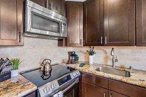 A kitchen with a stainless steel microwave, a gas stove, a sink, and wooden cabinets. - Stunning West Maui Oceanview Retreat (Honokowai)