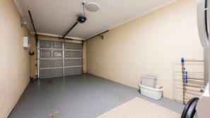 Un garatge amb un sòl gris, una paret blanca i una porta de garatge tancada de color gris. Hi ha una cistella blanca per a la roba i un escurabutaps metàl·lic.