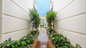 A narrow pathway flanked by lush greenery and a herringbone-patterned floor leading to a gated entrance. - Breakers 5/5- Stone Real Estate Yamba (Yamba)