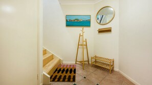 A hallway with a wooden staircase, a painting of a coastal scene, a mirror, and a wooden drying rack. - Breakers 5/5- Stone Real Estate Yamba (Yamba)