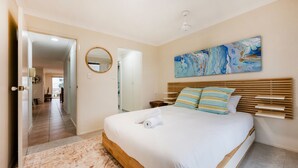 A bedroom with a bed, a wooden headboard, a painting, and a mirror on the wall. - Breakers 5/5- Stone Real Estate Yamba (Yamba)