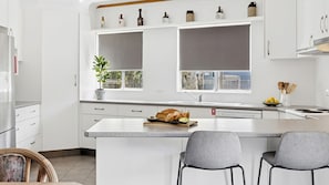 Una cocina moderna con armarios blancos, una isla central con asientos y vistas de la ciudad a través de las ventanas.