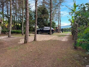 Un coche negro estacionado en un área boscosa con un sendero de tierra que lleva a un edificio.