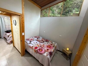 Ein Schlafzimmer mit einem Bett, einem kleinen Tisch, einem Fenster und einer Tür zu einem anderen Raum.
