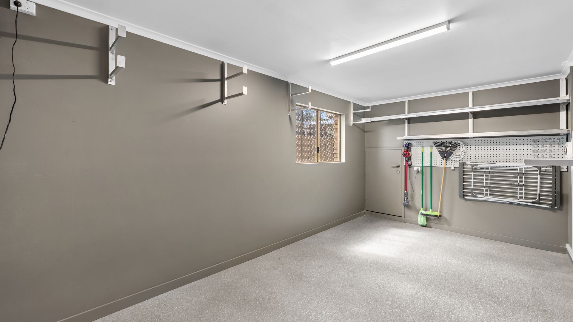 Una habitación limpia y bien iluminada, con una pared gris, una ventana con mosquitero y un techo con iluminación fluorescente.