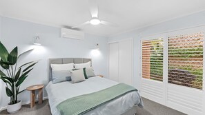 Ein Schlafzimmer mit einem Bett, Nachttischen, einem Deckenventilator, einer Klimaanlage und einem Fenster mit Jalousien.