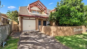 Ein Wohnhaus mit Garage, einer Ziegelmauer mit Namensschild, einem gepflasterten Einfahrtsweg und einem eingezäunten Garten.