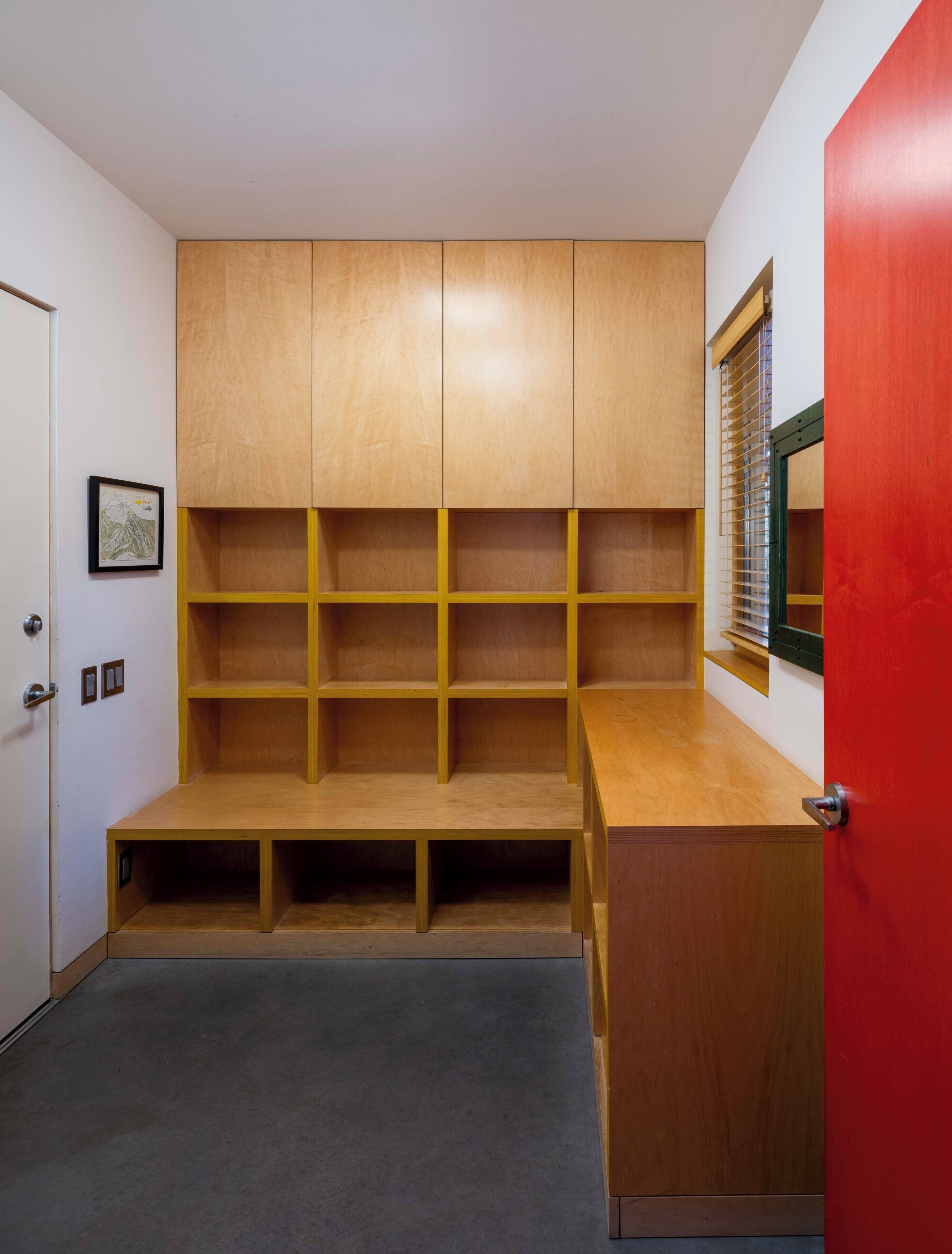 Ein Zimmer mit einer eingebauten Holzwandregal, einem kleinen Schreibtisch und einer roten Tür.