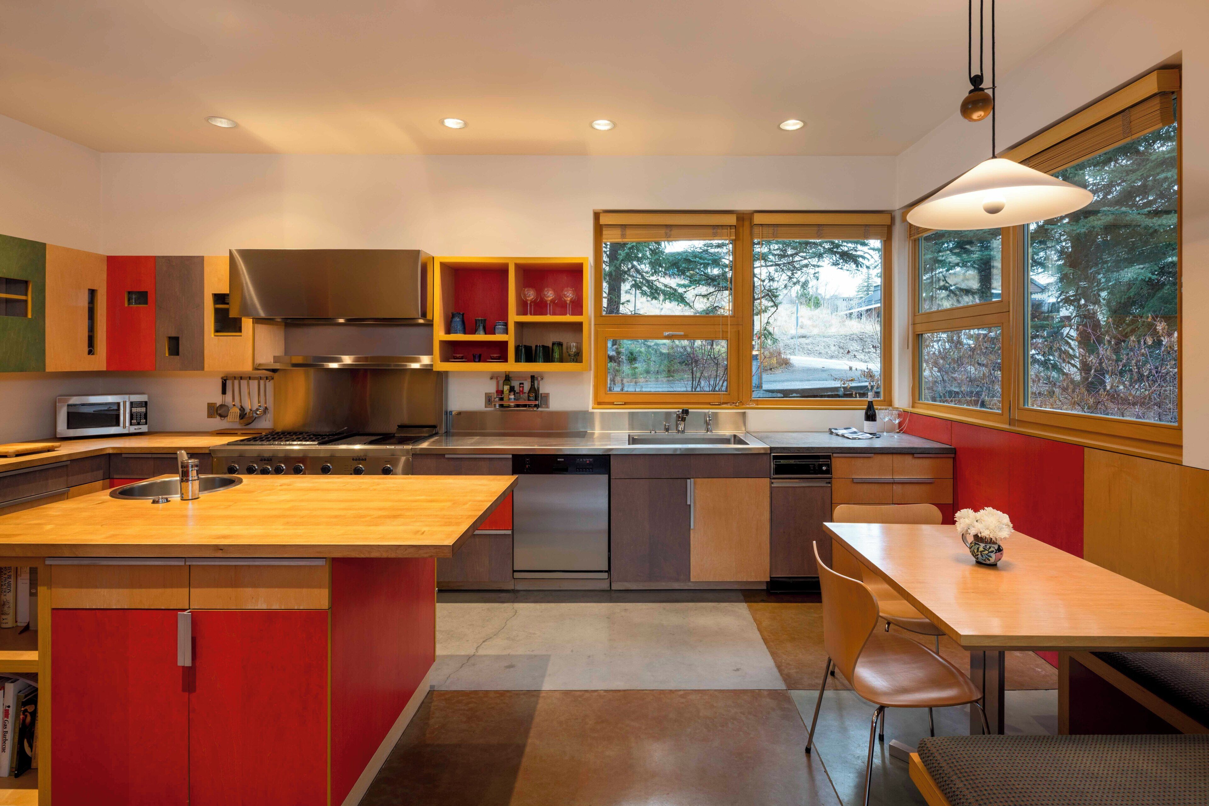 A modern kitchen with a central island, stainless steel appliances, and a large window offering a view of trees.