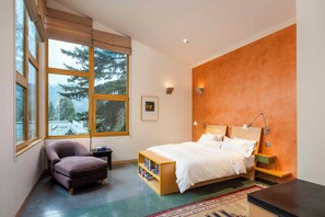 A modern bedroom with a large bed, a chair, a bedside table, and a view of trees through large windows. - The Gallery House | Architectural Digest–Featured Ketchum Home (Ketchum)