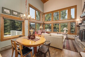 A spacious living area with a wooden dining table, comfortable seating, and large windows offering views of the outdoors.