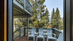 Una terraza de madera con sillas Adirondack blancas y vistas a árboles y montañas.