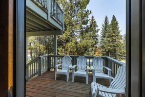 A wooden deck with white Adirondack chairs and a view of trees and mountains.