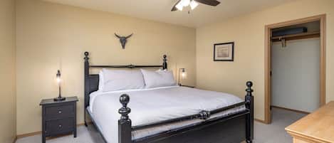 A bedroom with a bed, bedside tables, a ceiling fan, a wall-mounted bull skull decoration, and a framed picture.