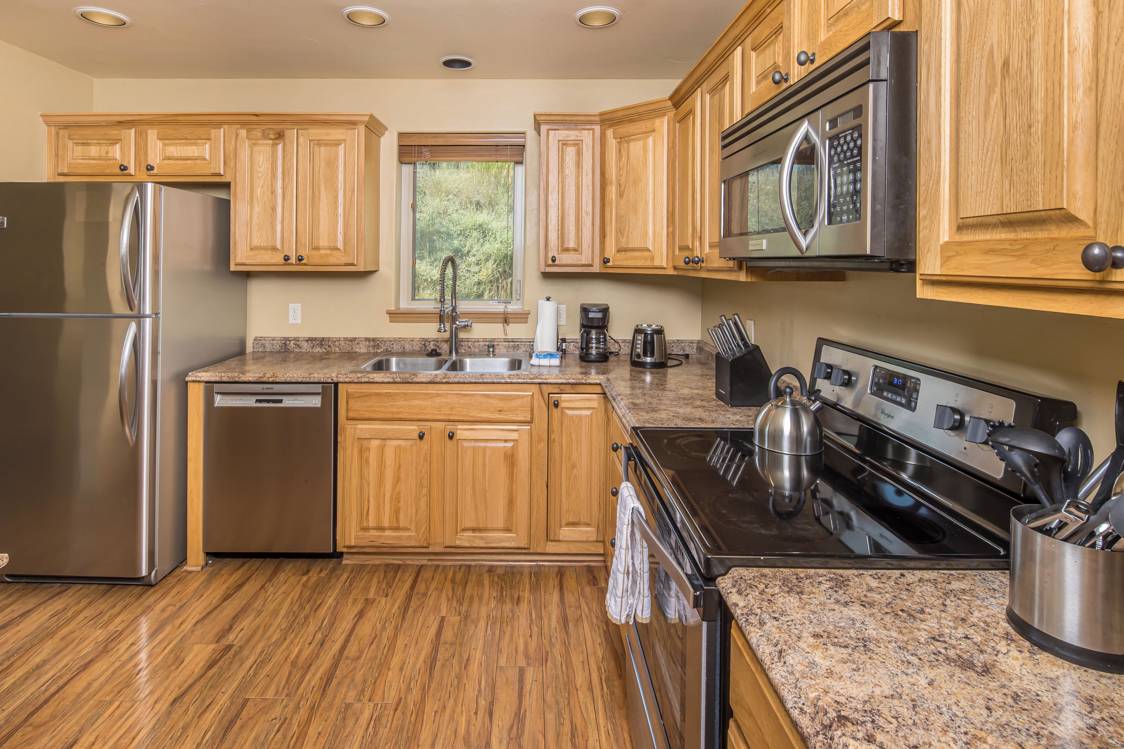 A modern kitchen with wooden cabinets, stainless steel appliances, granite countertops, and a window providing natural light.